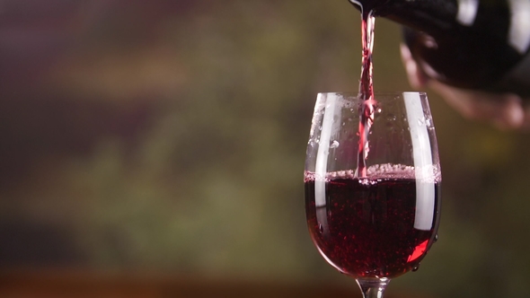 Person Pouring Red Wine from Bottle into Wine Glass