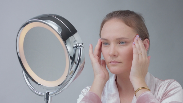 Caucasian Woman with Mirror with Ring Light with No Makeup Look Examine Her Skin and Makes Facial