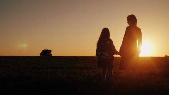 A Woman with a Girl Admires the Beautiful Sunset in a Picturesque Place. Silhouettes of Mom and