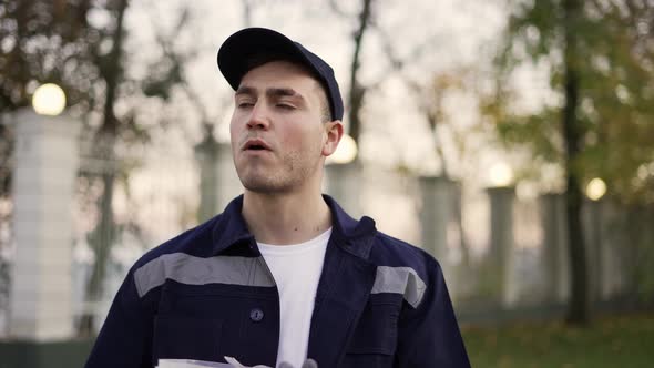 Relaxed Courier in Blue Uniform Enjoying Eating Food From Lunchbox and Standing in Autumn Street