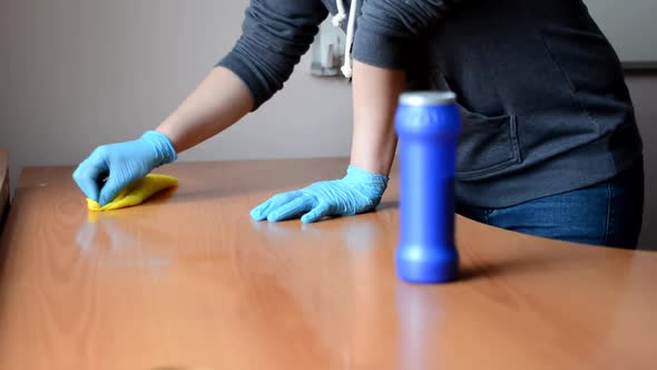 Girl in a Gray Sweater and Blue Gloves Washes a Wooden Table with a Yellow Rag