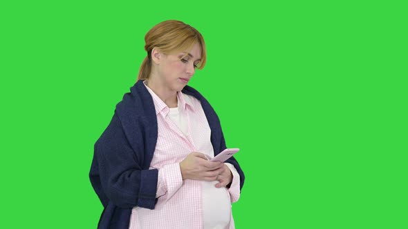 Pretty Pregnant Woman Using Her Smartphone Touching Her Belly Standing on a Green Screen, Chroma Key
