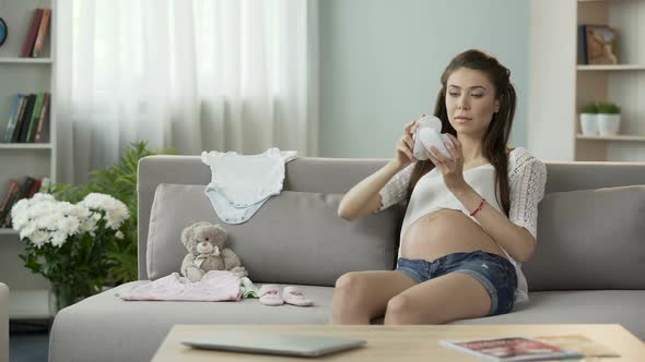 Young Pregnant Woman Taking a Look at Children Clothes on Sofa, Baby Fashion