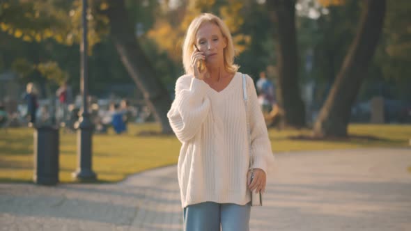 Beautiful Mature Woman Talking on Phone Walking in Autumn Park on Warm Sunny Day