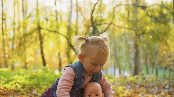Little Cute Baby Girl Playing with Doll in the Autumn Park