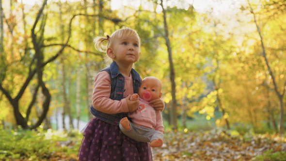 Little Cute Baby Girl Stand with Doll in the Park