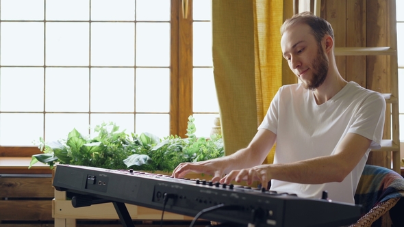 Cheerful Young Man in Casual Clothes Is Playing Keyboard at Home