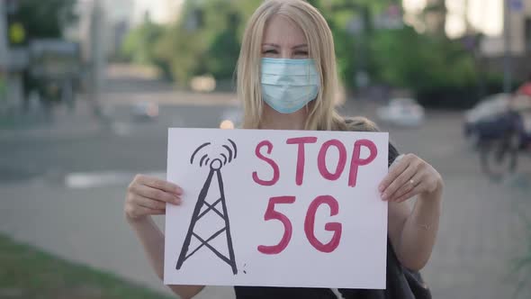 Blond Caucasian Woman in Face Mask Protesting Against 5G Mobile Towers. Rack Focus Changes From