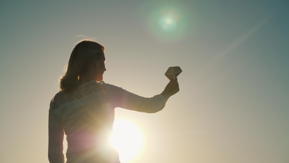 A Woman Is Playing with a Paper Airplane. It Stands in the Rays of the Setting Sun. Dreams About