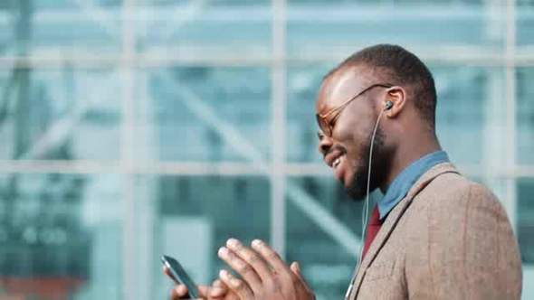 African American Businessman in the Sunglasses Talking on the Phone with Headphones Near the Office