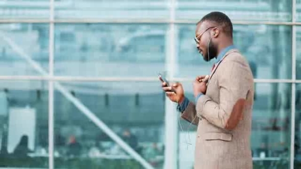 African American Businessman in the Sunglasses Talking on the Phone with Headphones Near the Office