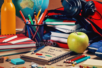 le. Recycle paper notebook, colored pencils, green apple, books, school backpack, black headphones, desktop world globe, and blue eraser. Back to school concept.