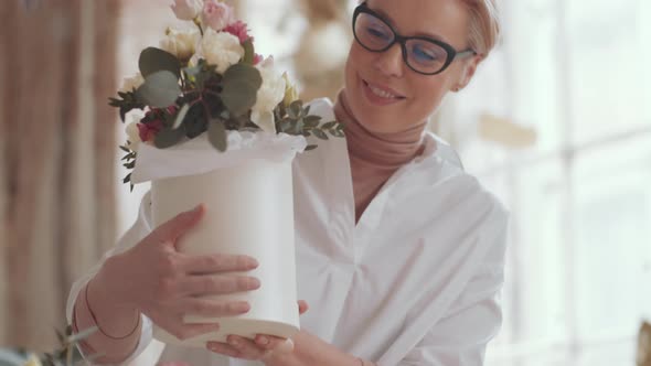 Joyous Mid-Aged Female Florist Holding Bouquet in Hatbox and Posing for Camera