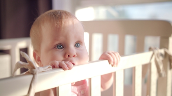 Baby Standing in Bed at Home. Portrait of Baby Girl Stand in Cot. Baby Eyes