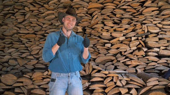 Portrait Of A Manly Man In A Cowboy Hat In Warehouse Holding A Bunch Of Firewood