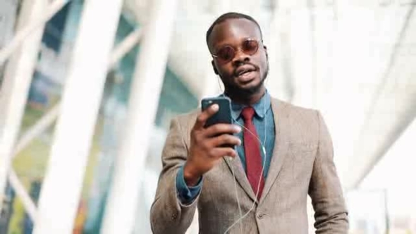 African American Businessman in the Sunglasses Talking on the Phone with Headphones Near the Office