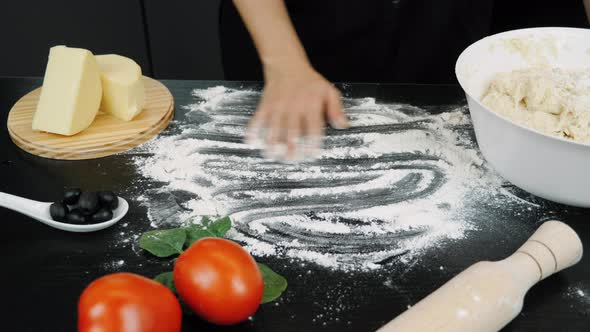 Cook's hand sprinkles flour on table. Pizza cooking