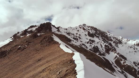 Aerial View of a Young Thin Man with a Backpack and Trekking Sticks Climbs Uphill on a Crest on the