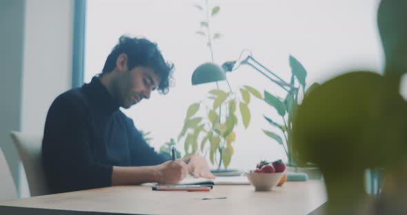 Young man with beard making notes while sitting at a table