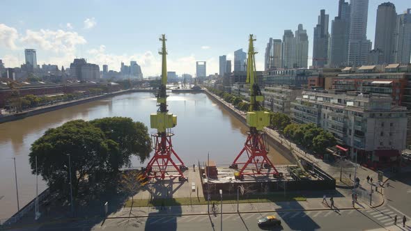 Aerial view of Puerto Madero waterway flying between cranes over a bridge. Dolly in