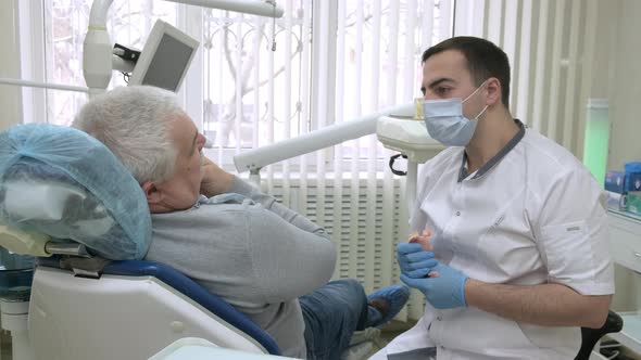 Male Dentist Consulting Elderly Patient Before Treatment in Dental Clinic