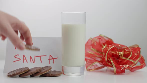 Closeup Milk in Glass and Hand Putting Cookie for Santa on Table