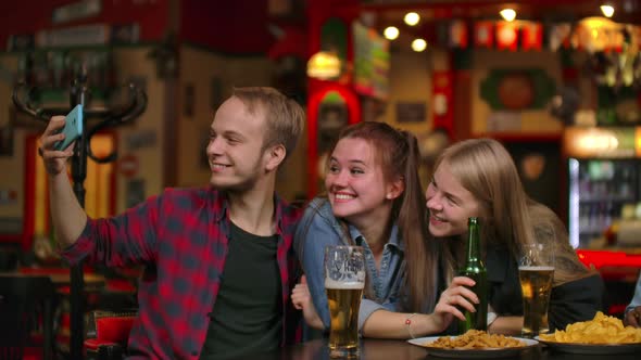 Group of Friends Man and Two Girls Take Selfie in a Bar Laughing and Smiling