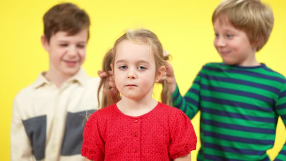 Portrait of Cute Little Girl Looking at Camera As Boys Pulling Pigtails at Yellow Background