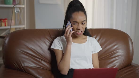 Angry Young African American Woman Talking on the Phone Sitting in Home Office with Laptop on