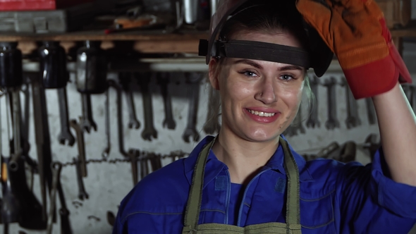 Cute Girl Welder in Uniform in the Garage in the Background of the Workbench