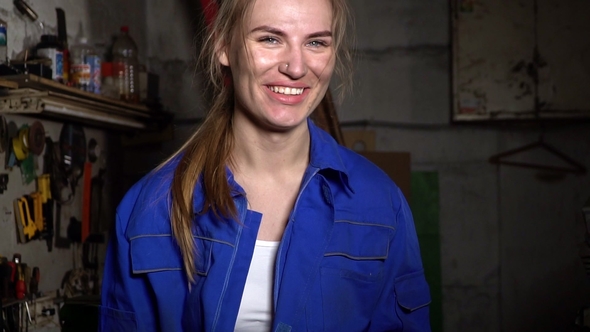 Cute Girl Mechanic in a Garage on the Background of the Instruments Smiling