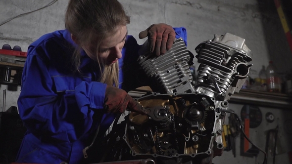 Cute Mechanic Girl in Uniform in the Garage Working with a Motorcycle Motor. Women's Work