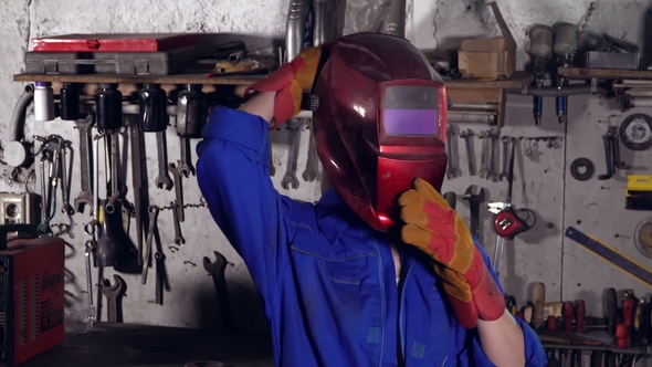 Girl Welder in Uniform in the Garage in the Background of the Workbench