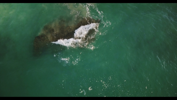 Drone Slowly Moving Over Transparent Green Sea Wave Crashing Over a Big Cay Reef Stone, Creating