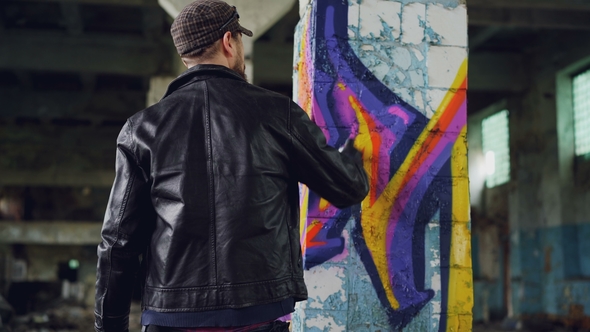 Rear View of Male Graffiti Artist in Leather Jacket Painting on Damaged Column Inside Empty