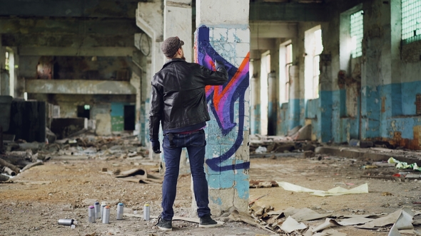 Back View of Graffiti Painter Creating Image with Aerosol Paint Inside Abandoned Building