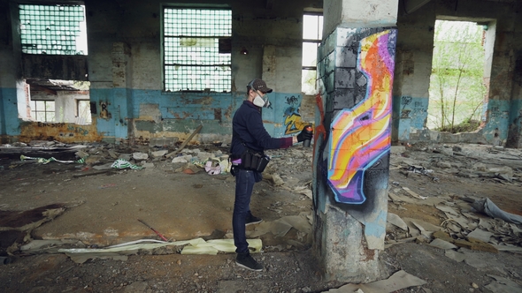 Male Graffiti Artist Is Decorating Old Damaged Column Inside Empty Industrial Building with Abstract
