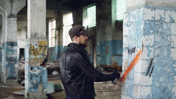 Bearded Graffiti Artist Is Painting on Pillar in Old Abandoned Building Using Aerosol Paint