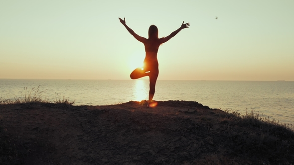 Silhouette of Woman Practicing Yoga on Hill Over Sea at Sunset. Meditation. Flexibility Workout at