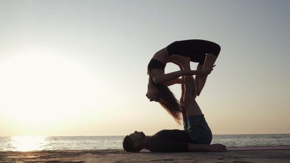 Silhouettes of Fit Young Couple Doing Acro-yoga at Sea Beach