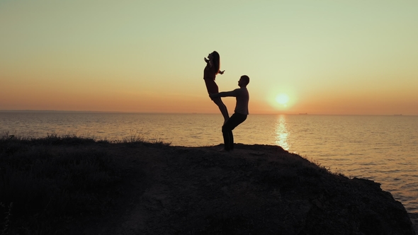 Silhouette of Young Woman and Man Doing Pair Yoga on Sea Beach at Sunset. Meditation