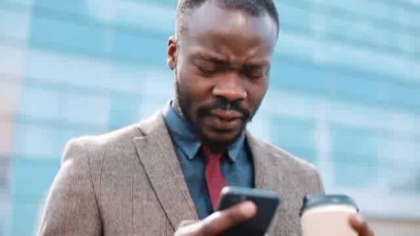 Tired and Stressed African American Businessman Reads Something in His Smartphone Standing Outside