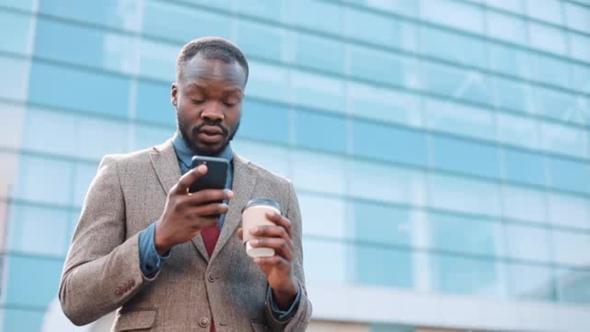 Tired and Stressed African American Businessman Reads Something in His Smartphone Standing Outside