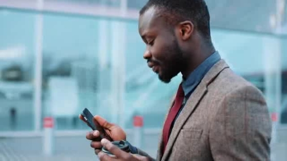 Tired and Stressed African American Businessman Uses a Smartphone Walking Down the Street