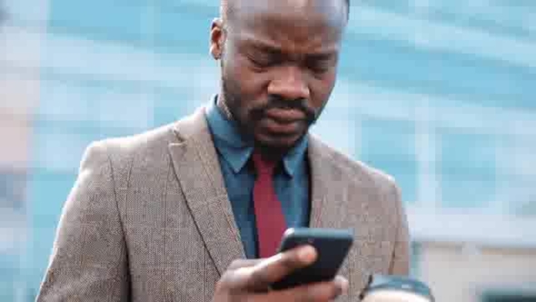 Tired and Stressed African American Businessman Reads Something in His Smartphone Standing Outside