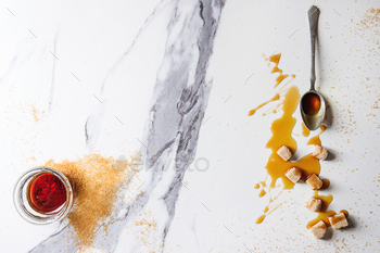 glass jar with spoon and cane sugar cubes over white marble background. Flat lay, space.