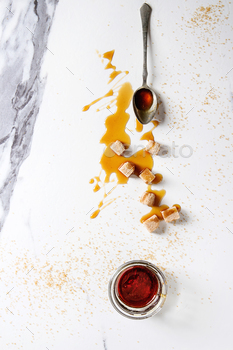  glass jar with spoon and cane sugar cubes over white marble background. Flat lay, space.