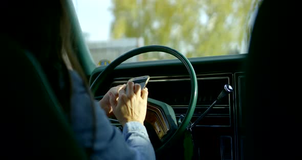 Close-up of a Dark-haired Woman Sitting Behind the Wheel of a Classic American Car and Looking Into