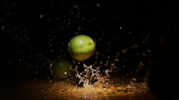 Citrus Limes Falling on Wet Surface in Orange Light Spot and Black Background