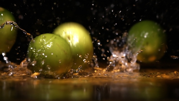 Lime Fruits Falling on Water Surface in Orange Light Spot and Cloud of Fog Splash and Drops